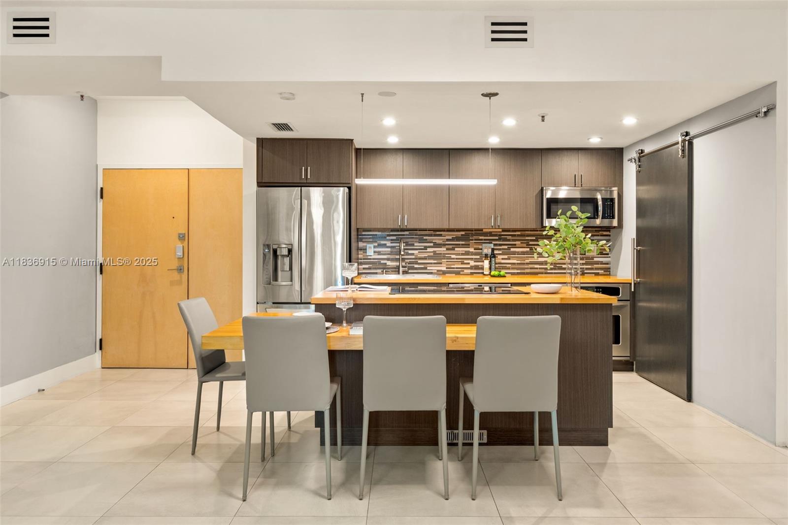 A modern kitchen features dark wood cabinetry, a wooden island countertop, and four gray chairs — 9755 NW 52nd St # 206, Doral FL 33178, DORAL, FL