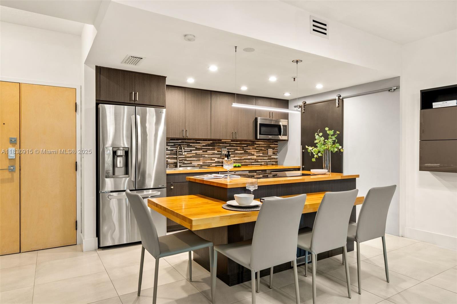 A modern kitchen features dark wood cabinets, stainless steel appliances, and a wooden island table — 9755 NW 52nd St # 206, Doral FL 33178, DORAL, FL