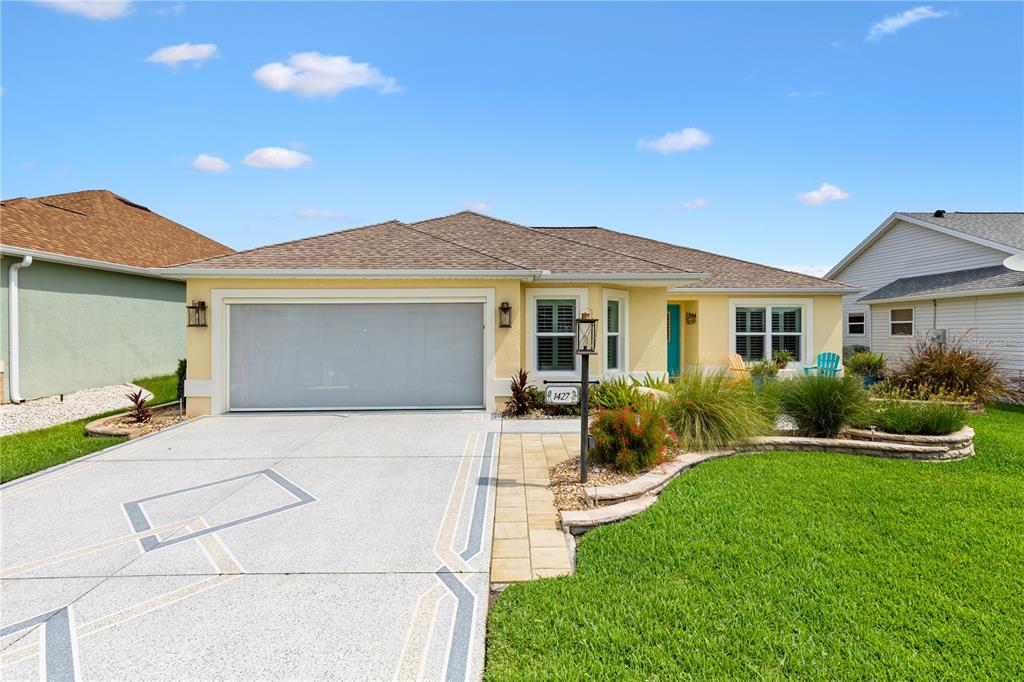 A single-story yellow house features a two-car garage, a paved driveway, and landscaped front yard — 1427 GAYLE MILL DRIVE, THE VILLAGES, FL