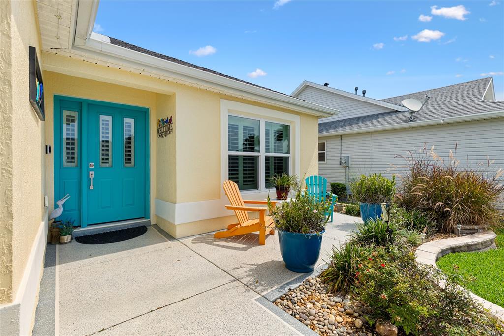 A yellow house exterior features a bright teal front door and a concrete patio area — 1427 GAYLE MILL DRIVE, THE VILLAGES, FL