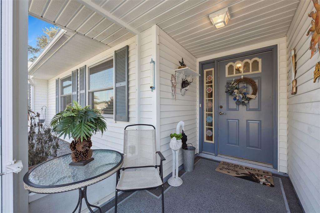 A covered front porch features a blue door, a small table with a plant, and a chair — 5636 LAVER STREET, LEESBURG, FL
