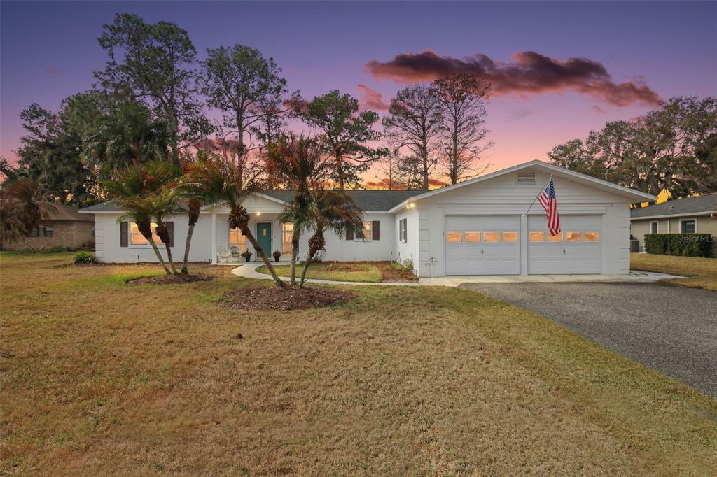 A single-story house with a white exterior, two-car garage, and palm trees on a lawn — 33225 LAKESHORE DRIVE, TAVARES, FL