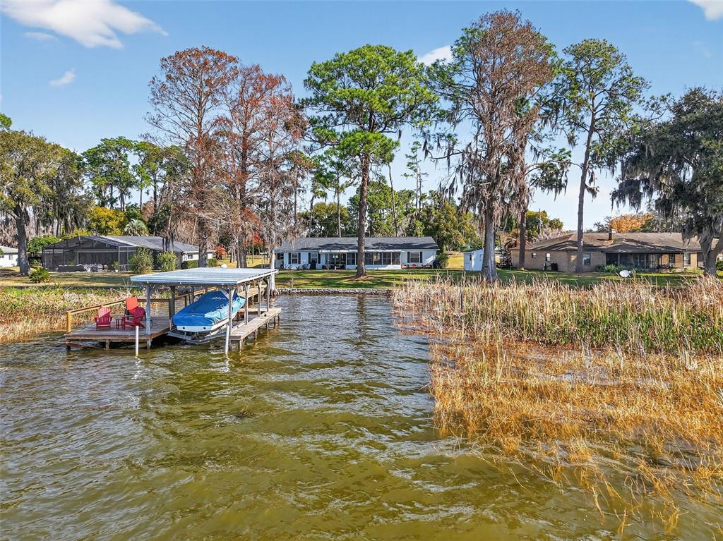 A boat dock with a covered slip sits on a lake in front of houses — 33225 LAKESHORE DRIVE, TAVARES, FL