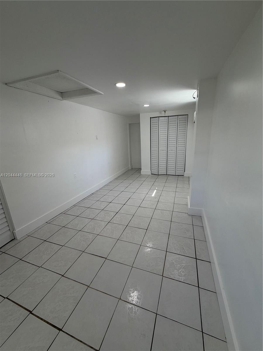 A narrow room features white walls, light-colored tiled flooring, and a white bi-fold closet door — NORTH MIAMI BEACH, FL