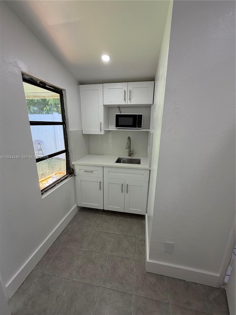 A small kitchenette features white cabinets, a stainless steel sink, and a microwave — NORTH MIAMI BEACH, FL