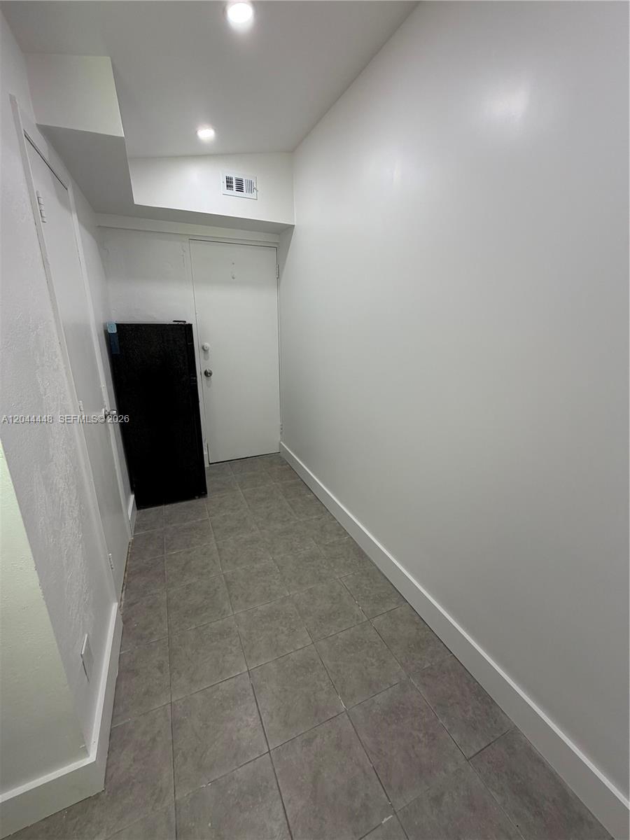 A small, empty room features gray tile flooring, white walls, and a black refrigerator — NORTH MIAMI BEACH, FL