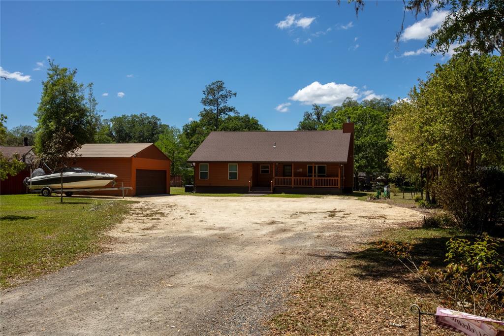 A single-story house with a porch and a detached garage sits on a dirt lot — 5930 ISLAND ROAD, MELROSE, FL