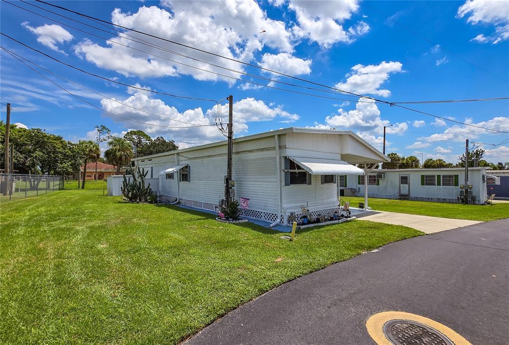 A white mobile home sits on a grassy lot next to an asphalt road — 6132 HARRIET STREET, ZEPHYRHILLS, FL