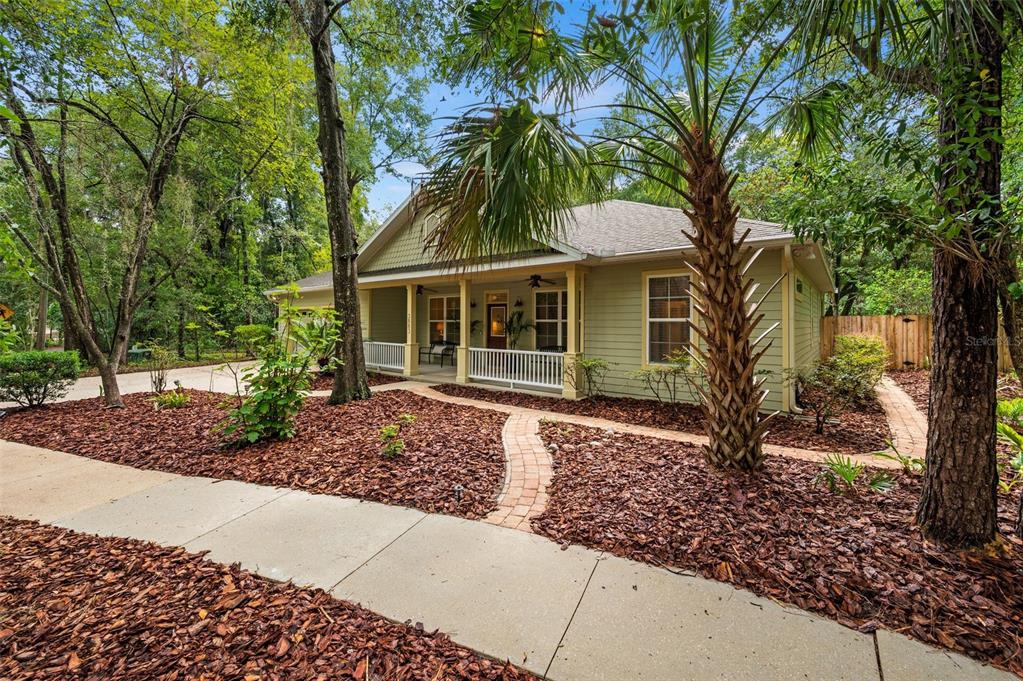 A light green house with a front porch and brick walkway surrounded by wooded landscaping — 3883 SW 21ST DRIVE, GAINESVILLE, FL
