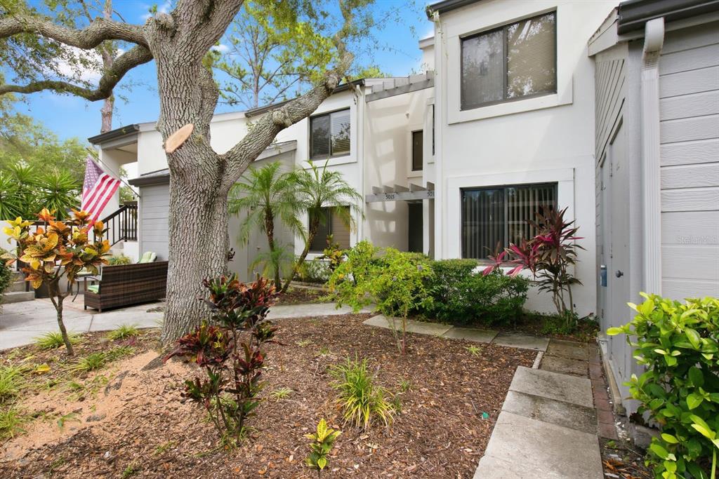 A two-story white townhouse exterior features a large tree, landscaping, and a paved walkway — 11440 HARBOR WAY UNIT 5013, LARGO, FL