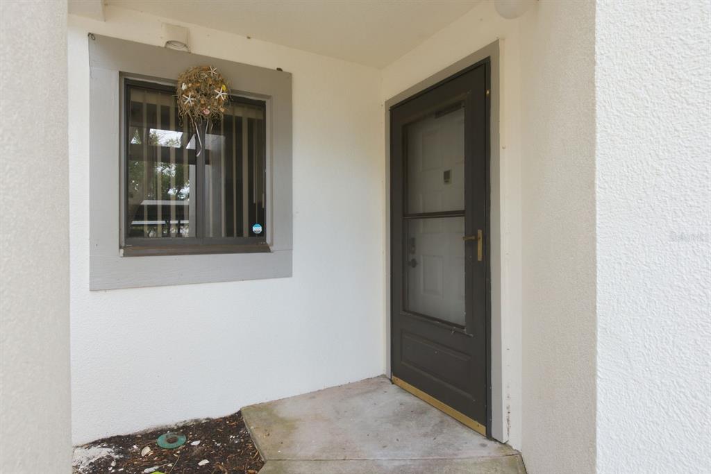 A concrete entryway features a dark-framed storm door and a window with a decorative wreath — 11440 HARBOR WAY UNIT 5013, LARGO, FL
