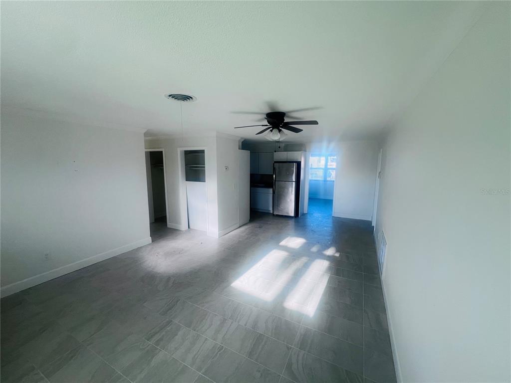 A living area with gray tile flooring, a ceiling fan, and an adjacent kitchen — 323 SCOTLAND DRIVE, DAYTONA BEACH, FL