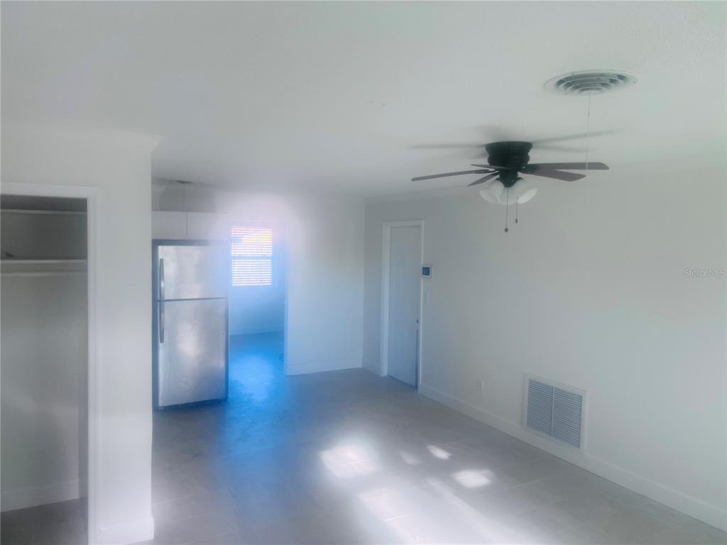 A bright room features white walls, tile flooring, a ceiling fan, and a stainless refrigerator — 323 SCOTLAND DRIVE, DAYTONA BEACH, FL