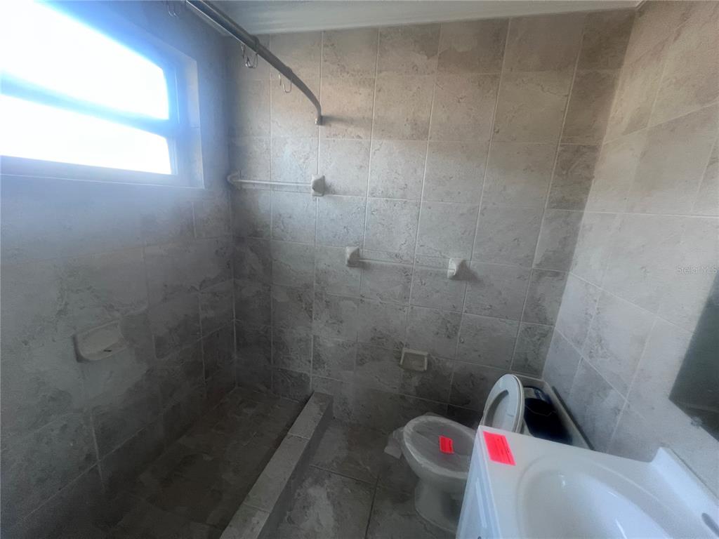 A bathroom features beige tiled walls, a shower area, a toilet, and a white vanity — 323 SCOTLAND DRIVE, DAYTONA BEACH, FL