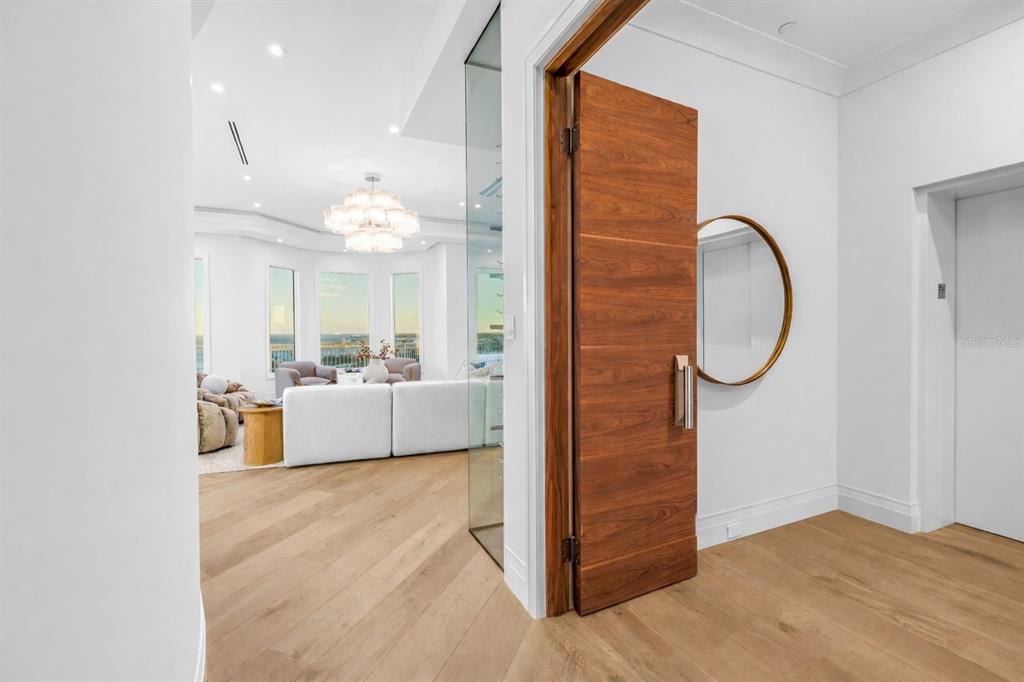 A wooden door opens into a bright living room with light wood floors and windows — 555 5TH AVENUE NE UNIT PH1, ST PETERSBURG, FL