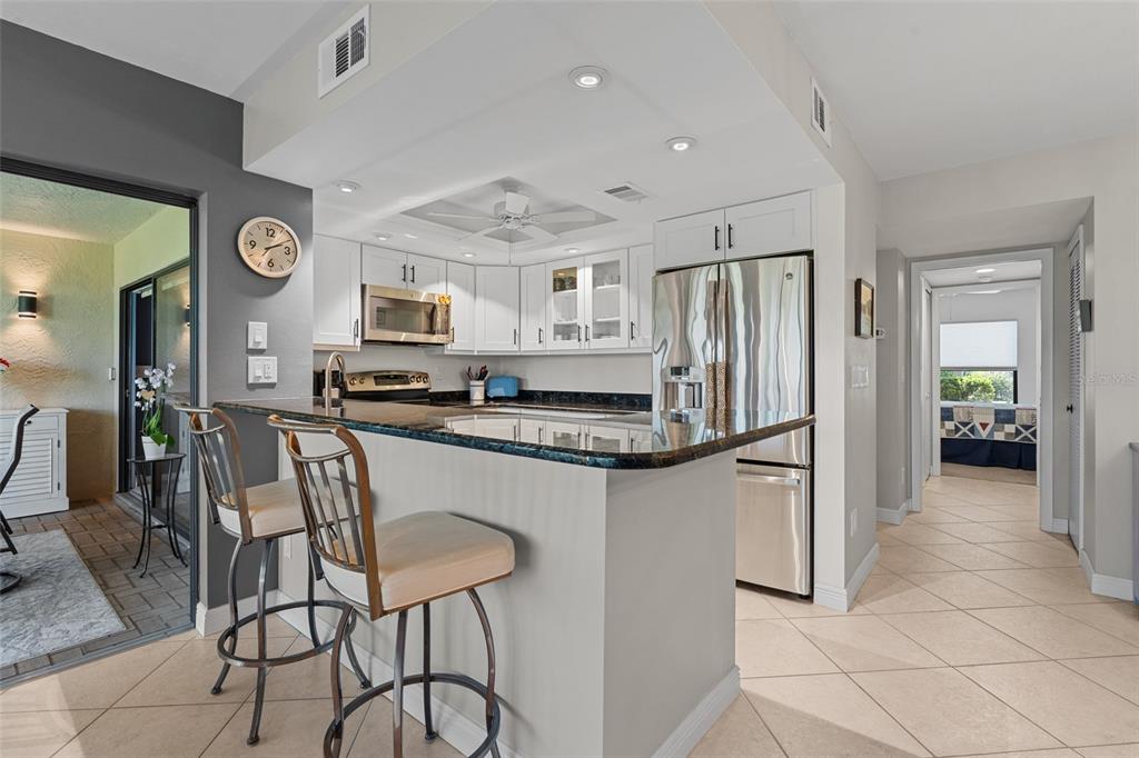 A kitchen features white cabinets, stainless steel appliances, a dark countertop, and two bar stools — 14770 EAGLE RIDGE DRIVE UNIT 112, FORT MYERS, FL