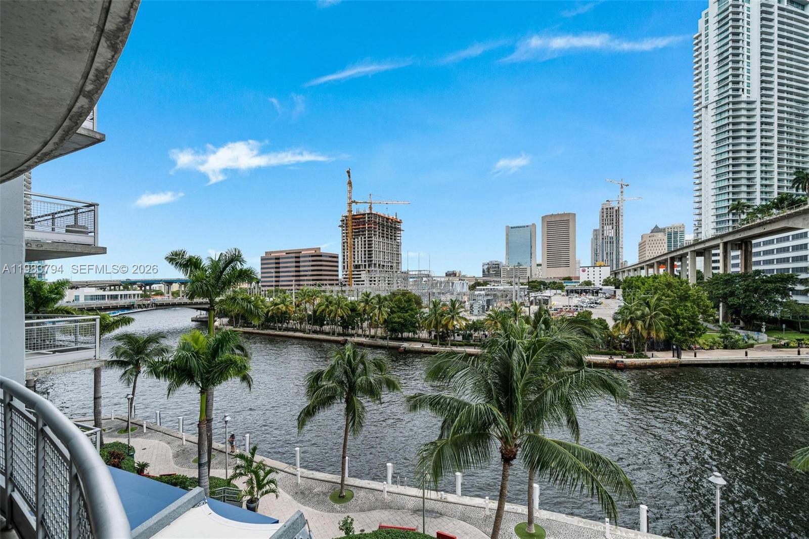 A balcony view overlooks a river, palm trees, and a city skyline with construction cranes — 690 SW 1st Ct # 501, Miami FL 33130, MIAMI, FL