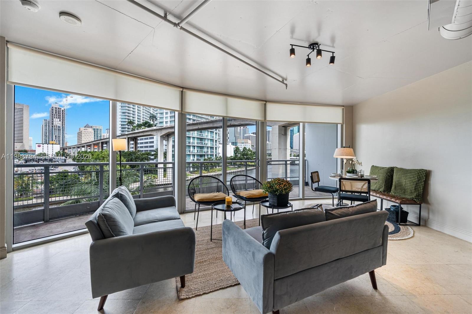 A living room features two grey sofas, modern chairs, and floor-to-ceiling windows overlooking a city — 690 SW 1st Ct # 501, Miami FL 33130, MIAMI, FL