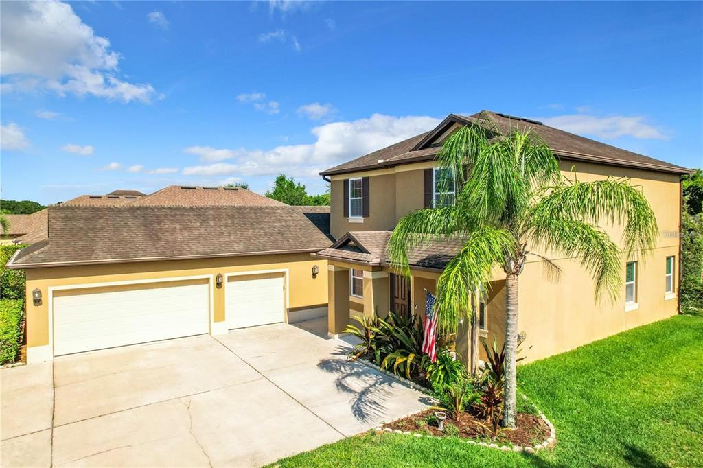 A two-story tan house with a three-car garage and a palm tree in front — 421 MEADOWRIDGE COVE, LONGWOOD, FL
