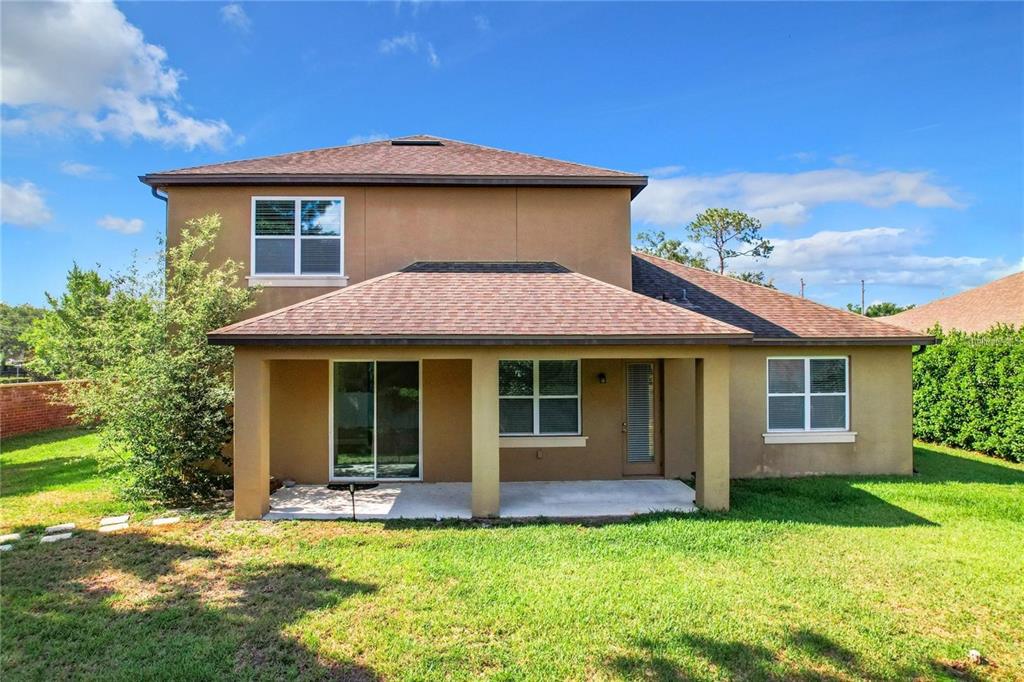 The rear exterior of a two-story tan house features a covered patio and lawn — 421 MEADOWRIDGE COVE, LONGWOOD, FL