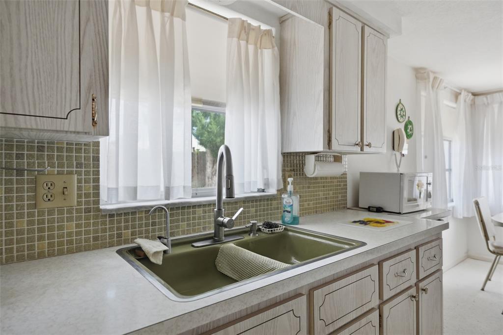 A galley kitchen with white cabinets, a green sink, and an adjacent dining area — 1207 LODESTAR DRIVE, HOLIDAY, FL
