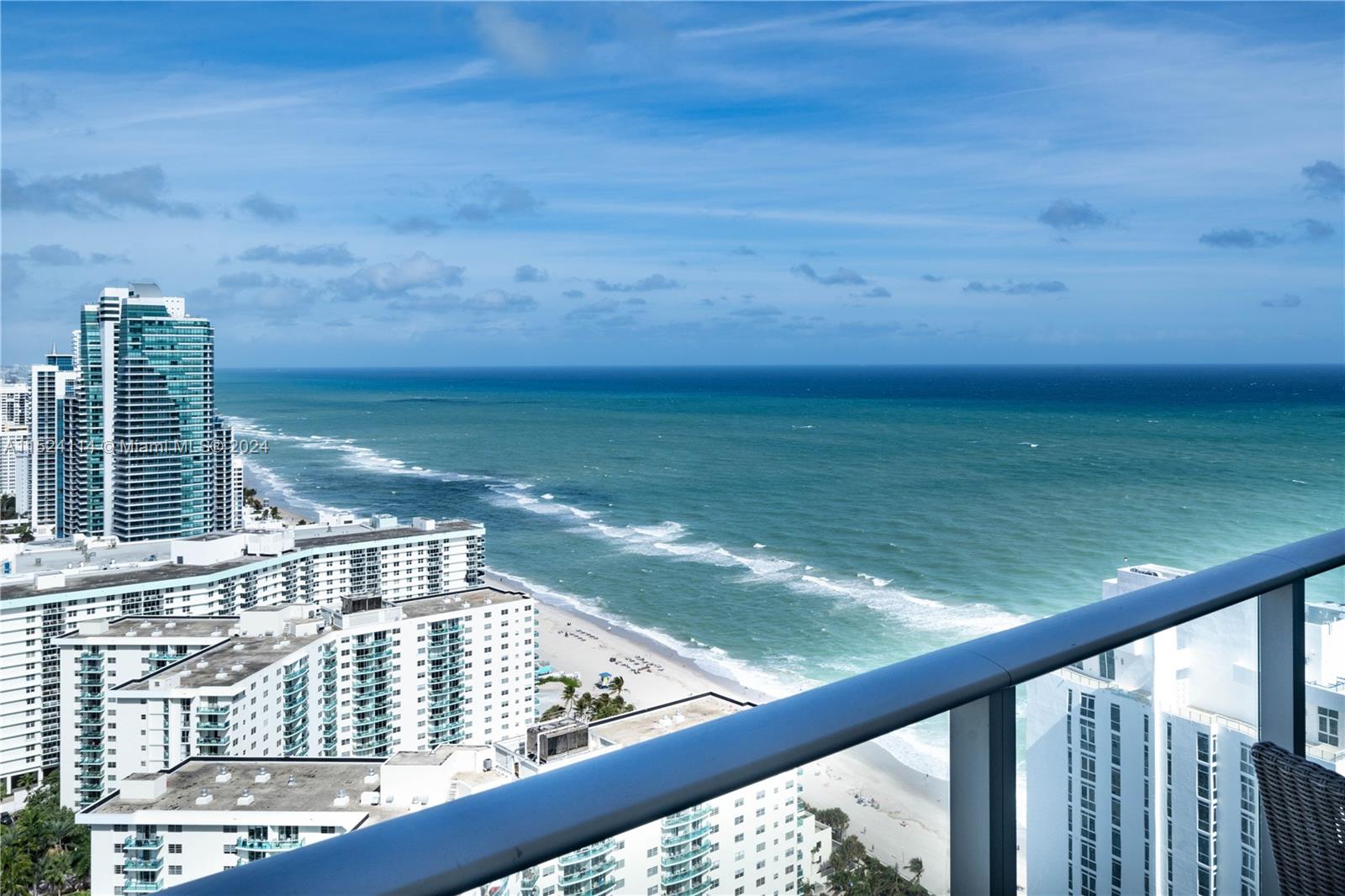 A high-angle view from a balcony overlooking a sandy beach, ocean, and coastal high-rise buildings — 4111 S Ocean Dr # 3112, Hollywood FL 33019, HOLLYWOOD, FL