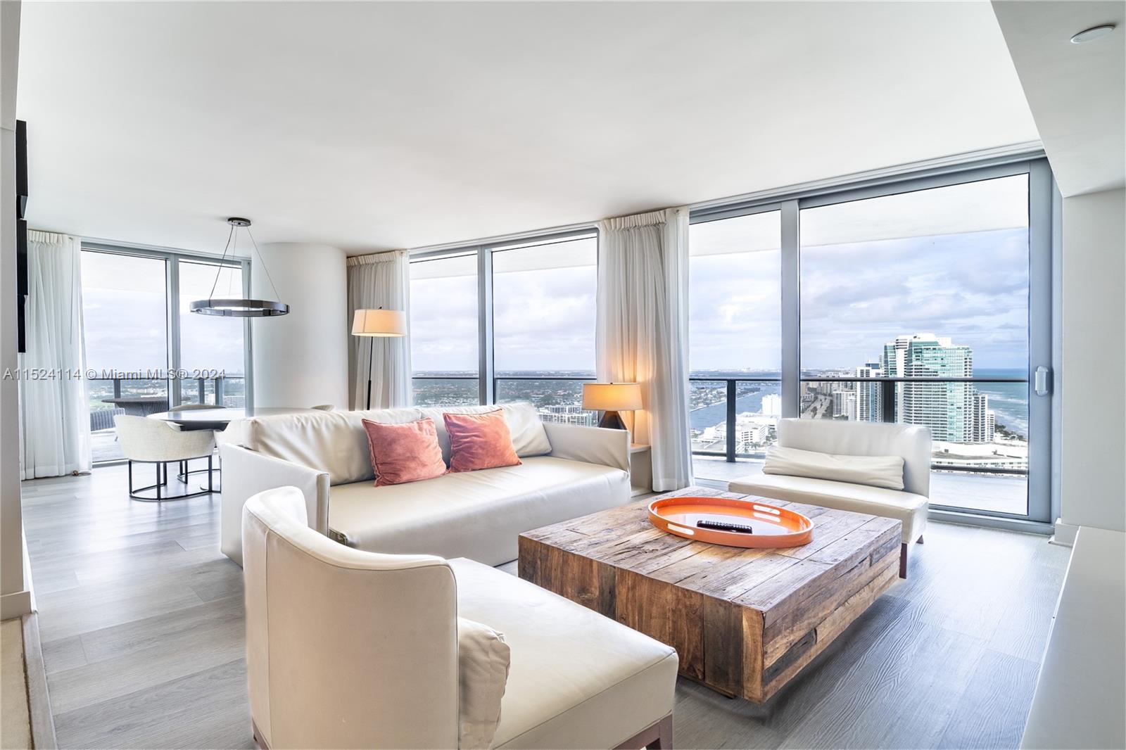 A modern living room features a white sofa, wooden coffee table, and floor-to-ceiling windows — 4111 S Ocean Dr # 3112, Hollywood FL 33019, HOLLYWOOD, FL