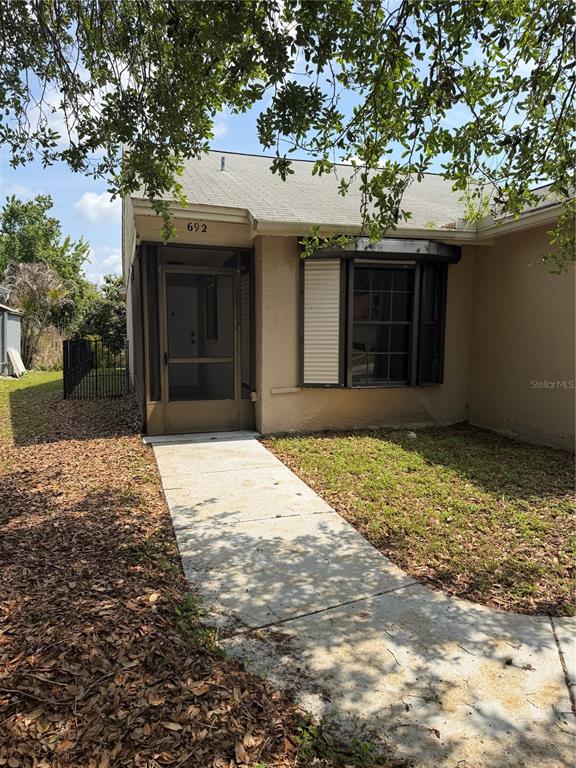A tan house exterior features a screened front entryway and a bay window — 692 BELLINGHAM PLACE, PALM HARBOR, FL