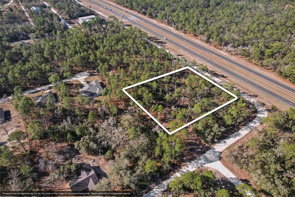 An aerial view shows a wooded, rectangular plot of land outlined in white near a highway — 17496 NICASIO JAY AVENUE, WEEKI WACHEE, FL