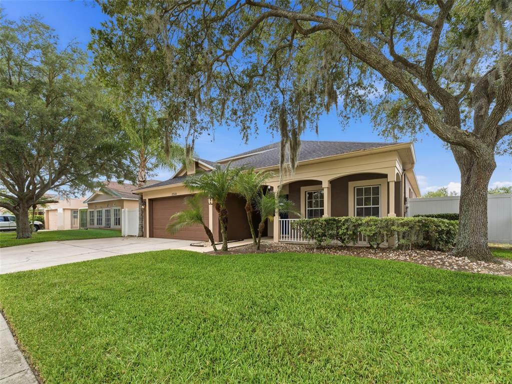 A single-story house with a brown garage, front porch, and large oak trees in front — 22536 LAURELDALE DRIVE, LUTZ, FL