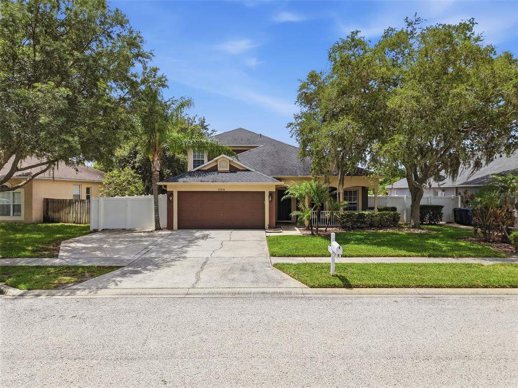 A two-story suburban house with a brown garage, a concrete driveway, and mature trees — 22536 LAURELDALE DRIVE, LUTZ, FL