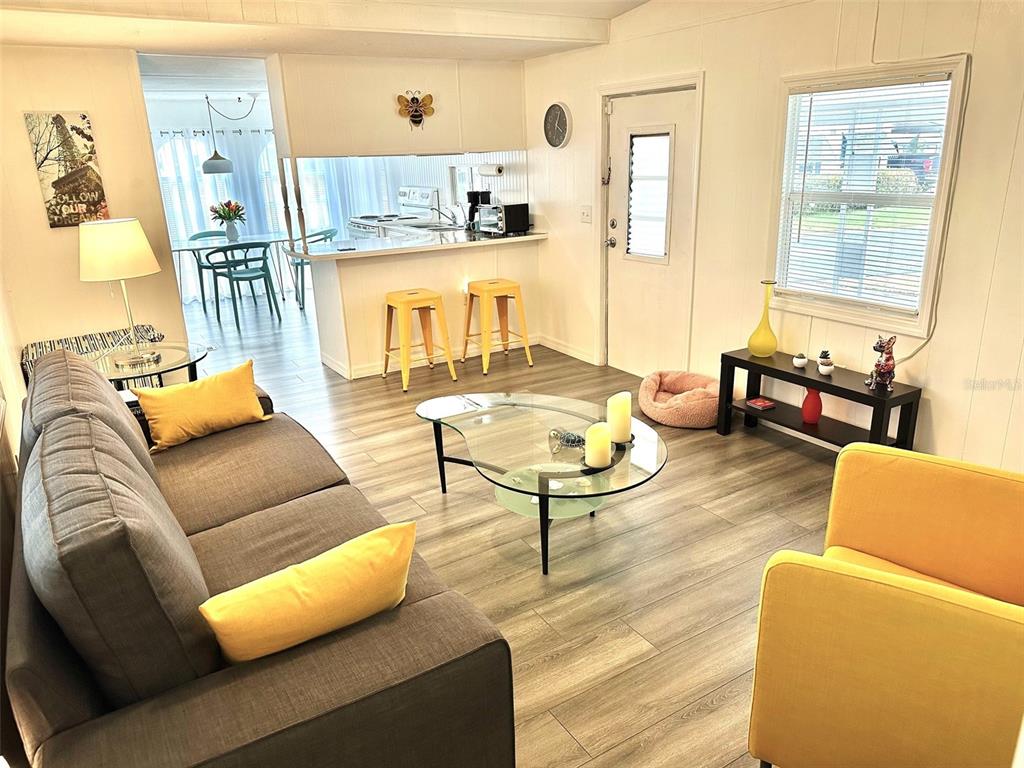 A living room with gray sofa, yellow chairs, glass coffee table, and an open kitchen — 9790 66TH STREET N UNIT 194, PINELLAS PARK, FL