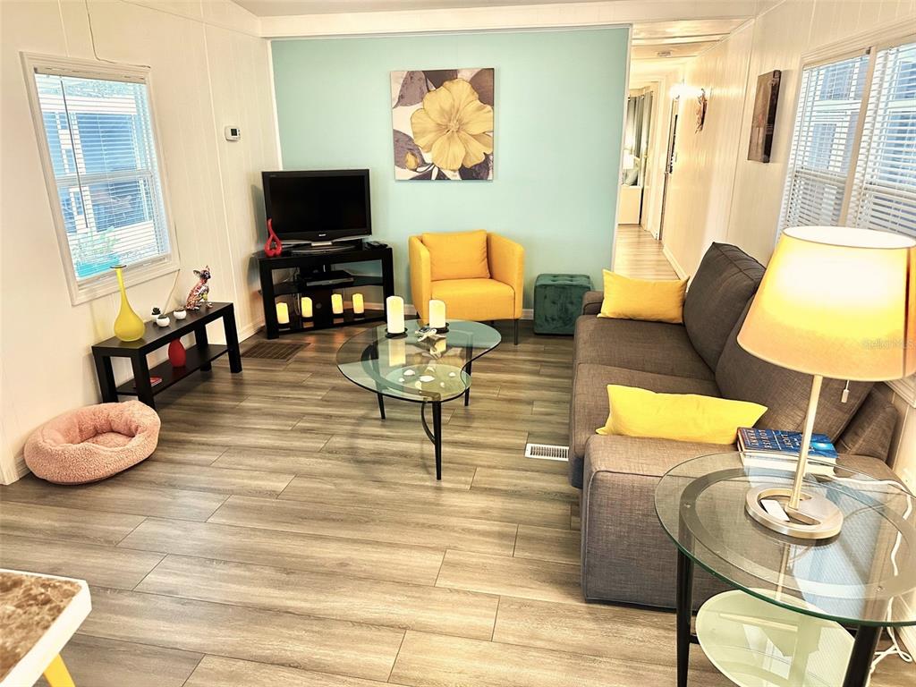 A living room features a grey sofa, yellow armchair, glass coffee table, and wood-look flooring — 9790 66TH STREET N UNIT 194, PINELLAS PARK, FL