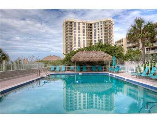 A swimming pool with lounge chairs and a thatched-roof cabana in front of a high-rise building — 2425 GULF OF MEXICO DRIVE UNIT 4E, LONGBOAT KEY, FL