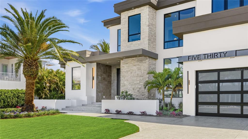 A modern two-story house features white stucco, stone accents, a palm tree, and a garage — 530 CHIPPING LANE, LONGBOAT KEY, FL