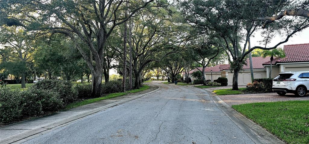 A paved residential street lined with large trees and houses with red tile roofs — 4026 LYNDHURST COURT UNIT 13, SARASOTA, FL