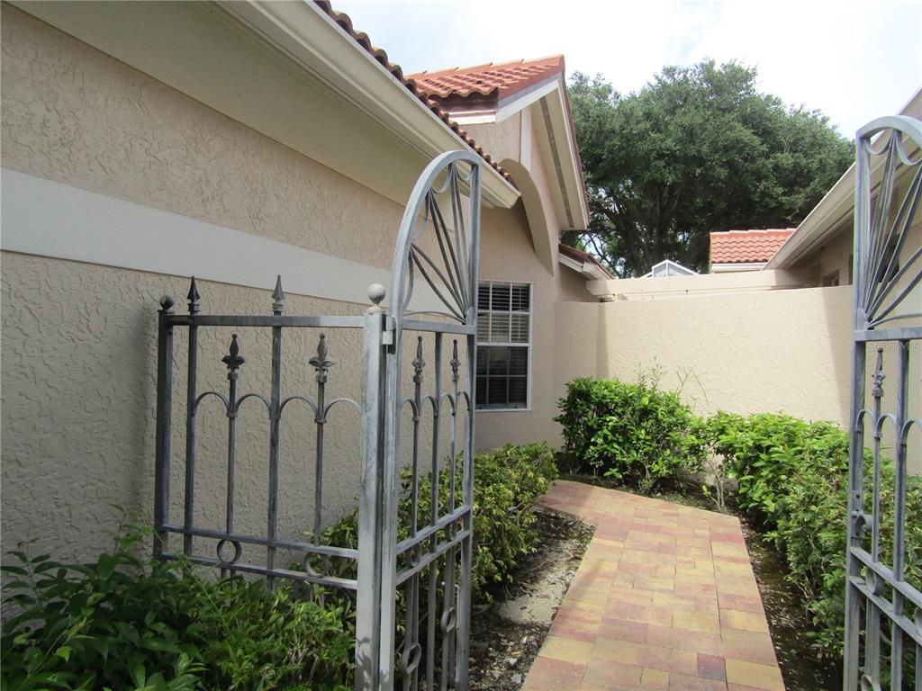 A metal gate opens to a paved walkway leading toward the side of a stucco house — 4026 LYNDHURST COURT UNIT 13, SARASOTA, FL