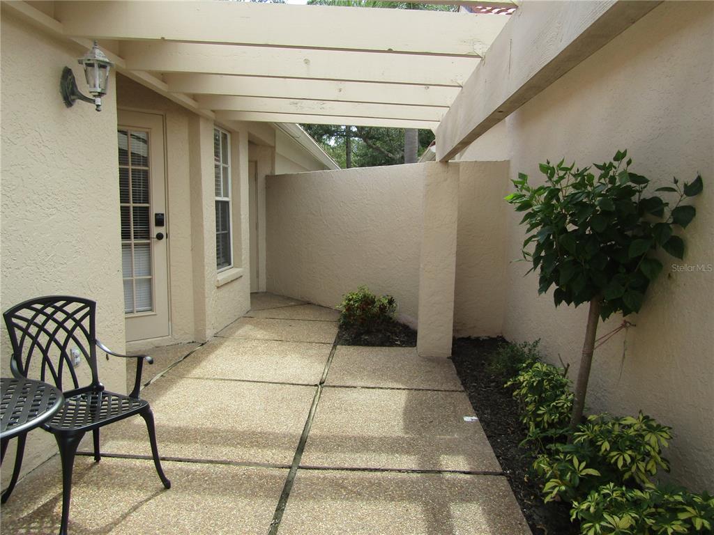 A patio features a concrete slab, a pergola, a black metal chair, and landscaping — 4026 LYNDHURST COURT UNIT 13, SARASOTA, FL