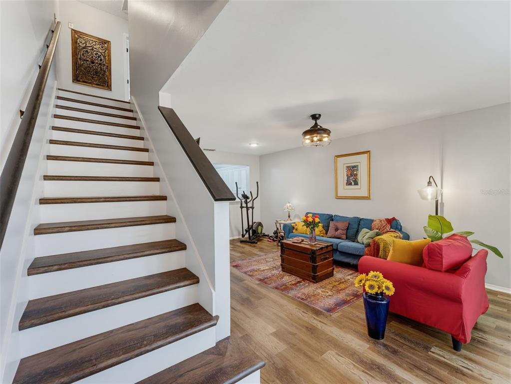 A living room with wood-look flooring, a blue sofa, a red armchair, and a staircase — 5100 BURCHETTE ROAD UNIT 905, TAMPA, FL