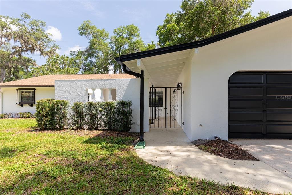 The exterior of a white house features a black garage door and a gated courtyard entrance — 515 TIVOLI COURT, ALTAMONTE SPRINGS, FL