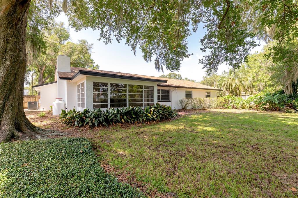 A white single-story house with a large window wall sits in a grassy, tree-shaded yard — 515 TIVOLI COURT, ALTAMONTE SPRINGS, FL