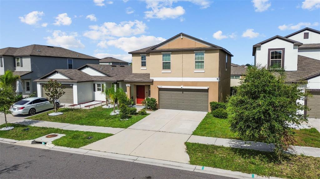 A two-story suburban house with a tan stucco exterior, a two-car garage, and a red door — 16671 KINGMAN REEF STREET, WIMAUMA, FL