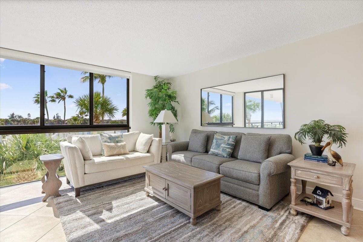 A living room features a beige sofa, a grey sofa, a coffee table, and large windows — 2800 N Highway A1a # 307, Fort Pierce FL 34949, FORT PIERCE, FL
