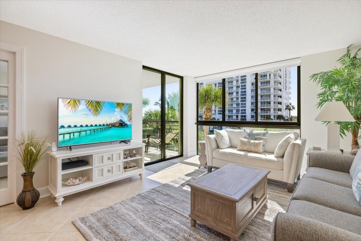 A living room features a television on a white stand, two sofas, and large windows — 2800 N Highway A1a # 307, Fort Pierce FL 34949, FORT PIERCE, FL
