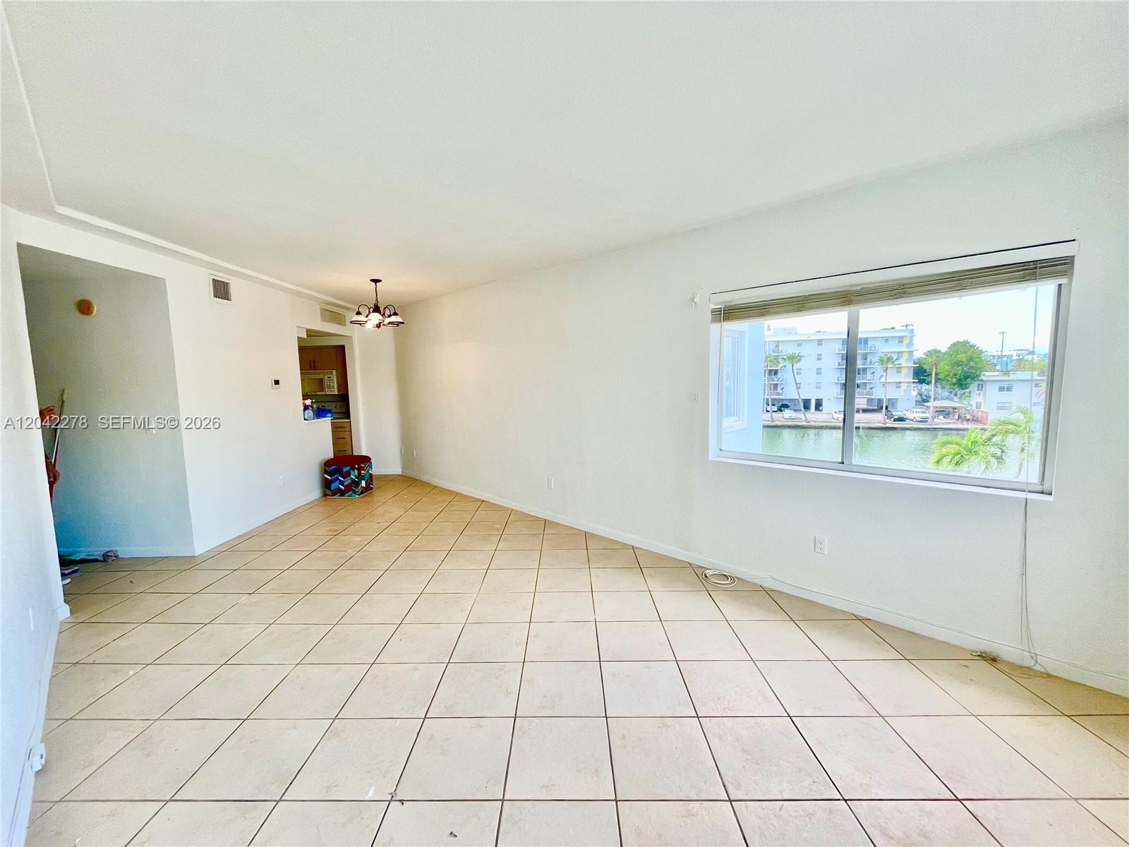 An empty room with tiled floors and a large window overlooking a canal and buildings — 1185 Marseille Dr # 309, Miami Beach FL 33141, MIAMI BEACH, FL