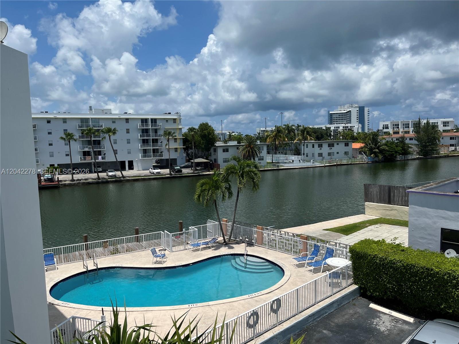 An elevated view shows a swimming pool and patio overlooking a canal with apartment buildings — 1185 Marseille Dr # 309, Miami Beach FL 33141, MIAMI BEACH, FL