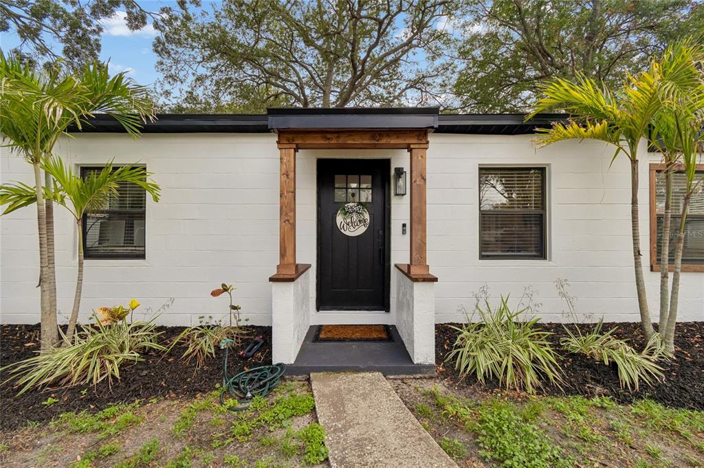 A white concrete block house features a black front door with a wooden porch frame — 4730 W BAY VISTA AVENUE, TAMPA, FL