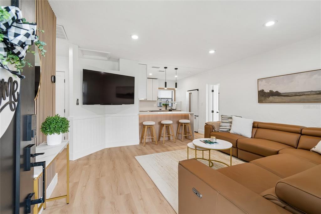 A modern living room features a tan leather sectional, a wall-mounted television, and an open kitchen — 4730 W BAY VISTA AVENUE, TAMPA, FL