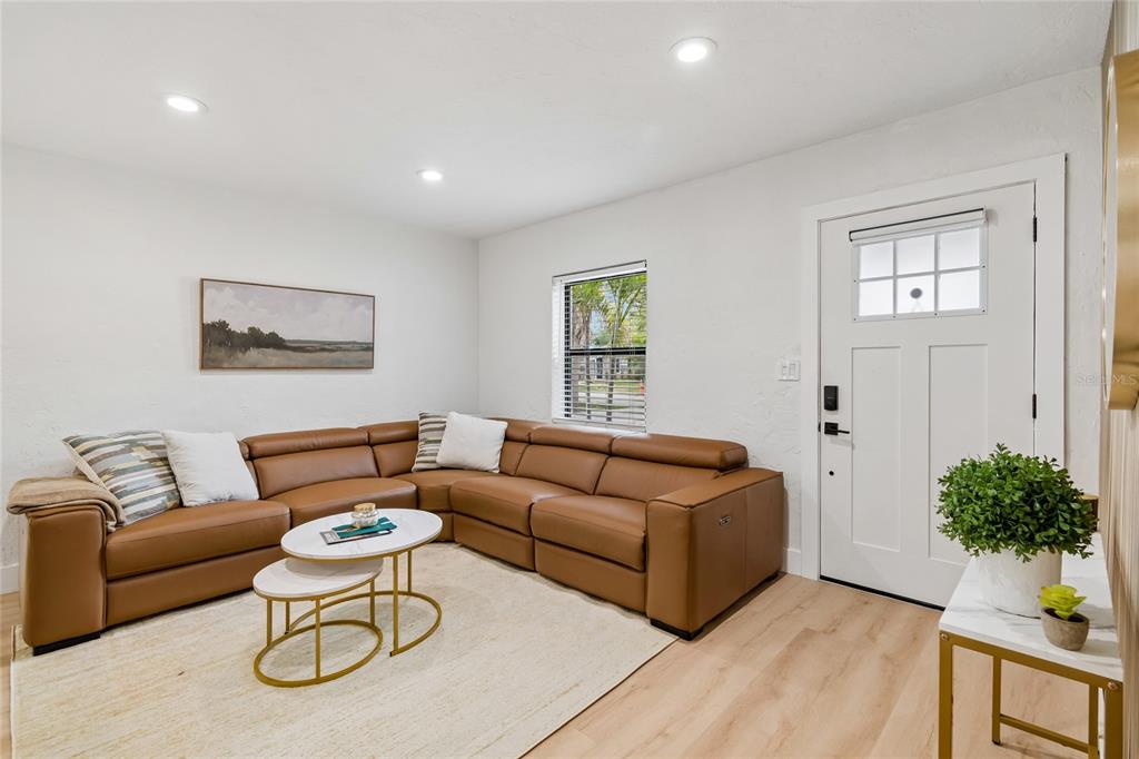 A living room features a brown leather sectional, nested coffee tables, and a white door — 4730 W BAY VISTA AVENUE, TAMPA, FL