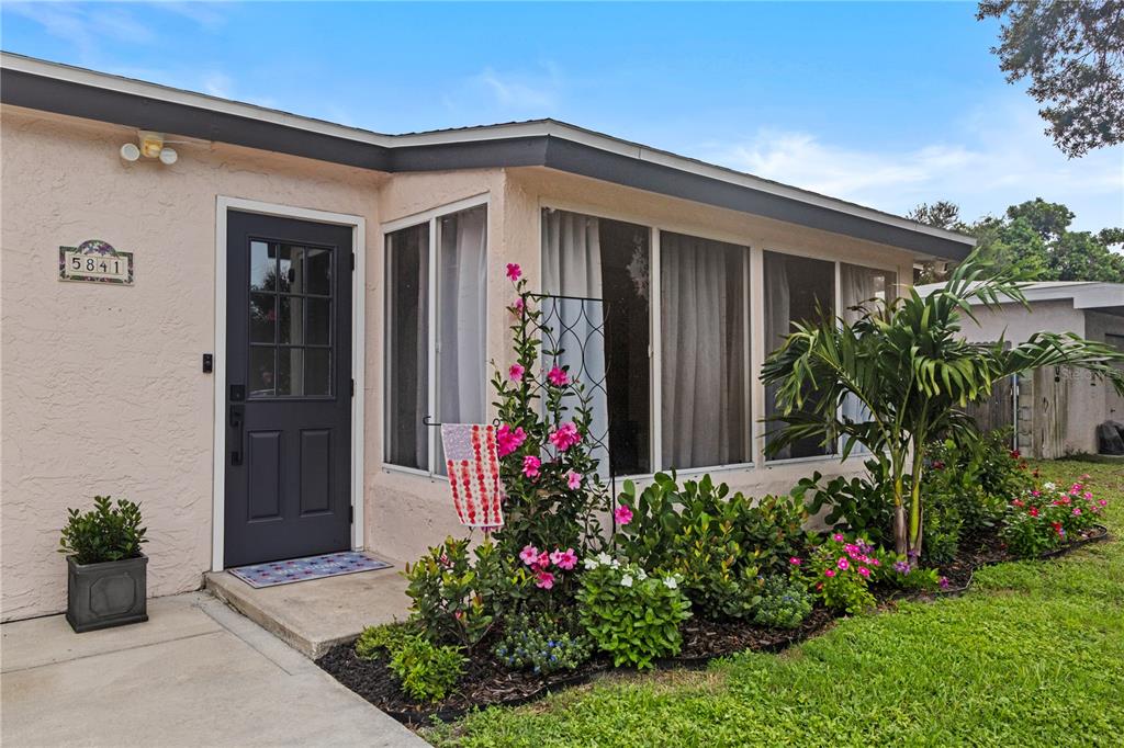 The exterior of a light-colored house features a dark door, large windows, and garden landscaping — 5841 67TH AVENUE N, PINELLAS PARK, FL
